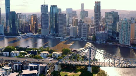 vehicles travelling across story bridge over brisbane river at sunset with high rise buildings at brisbane cbd, queensland, australia