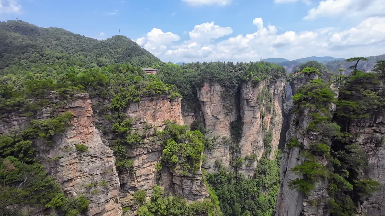 Camera pans right showing forested cliffs and vertical rock formations in Zhangjiajie National Park on a sunny day