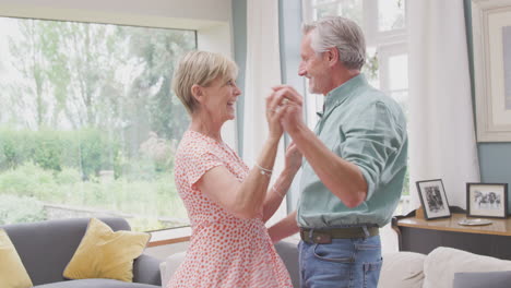 romantic senior retired couple dancing in lounge at home together