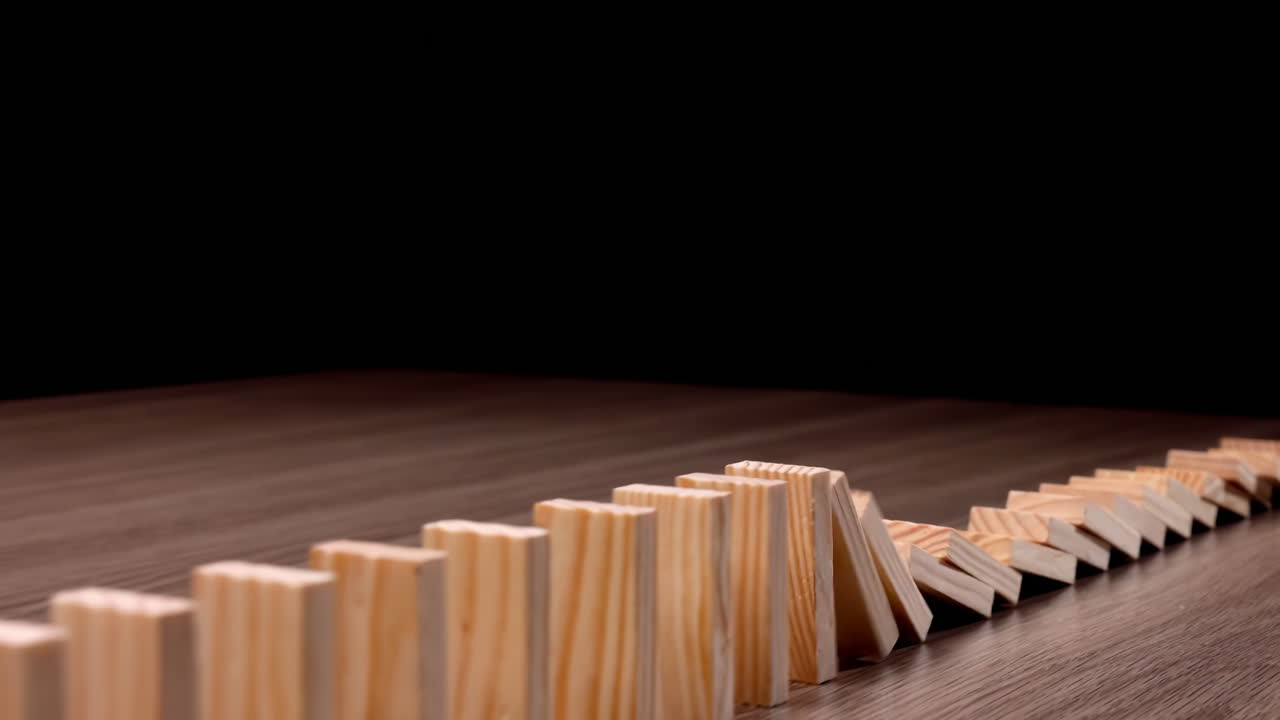 Una fila di domino di legno che cadono a catena, effetto domino continuo, prevenzione e sviluppo verso la stabilità, strategia aziendale e gestione del rischio