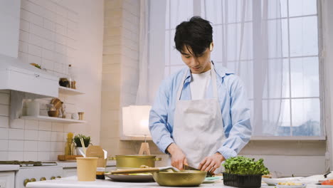 Japanese-Man-Cutting-Ingredients-In-The-Kitchen,-Then-Looks-At-The-Camera-And-Smiles