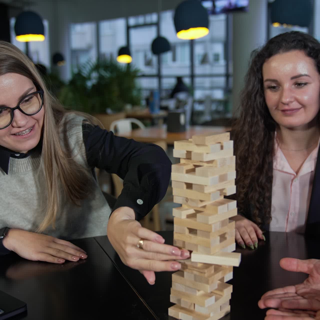 Company of friends playing jenga and having fun. One of the girls carefully pushes the brick in the pile of jenga. Leisure time for adults