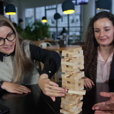 company of friends playing jenga and having fun. one of the girls carefully pushes the brick in the pile of jenga. leisure time for adults