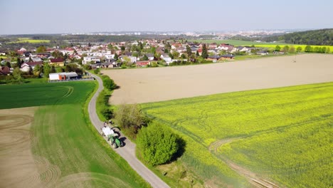 scenery view of vast field with furrows located near village houses under hill in daylight in countryside