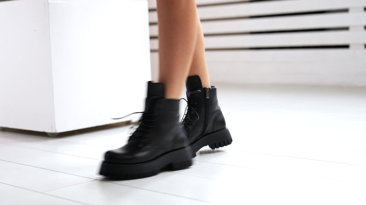 Girl with bare legs and black boots starts to jump. Model demonstrating the stylish leather footwear with laces at white backdrop. Close up.