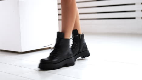 girl with bare legs and black boots starts to jump. model demonstrating the stylish leather footwear with laces at white backdrop. close up.