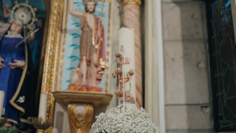 liturgical candle with detailed decorations and floral base in sacred setting