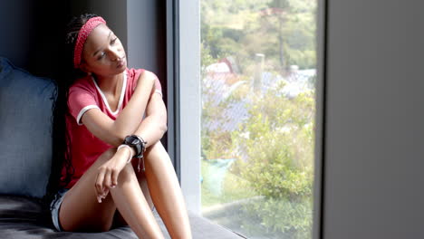 a young african american woman sitting by window, looking outside