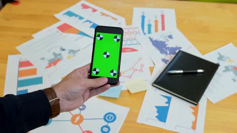 man using smart phone with green screen on office desk, work space, information look up