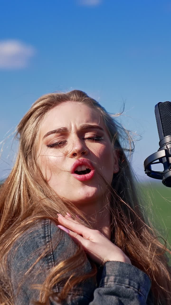 Girl singing in green field. Beautiful woman singing with microphone in green field. Vertical video