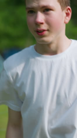 un primer plano de un niño joven intensamente enfocado y preparándose para bloquear una pelota entrante mientras está de pie cerca del poste de la portería, con una vista borrosa de equipos al aire libre en el fondo