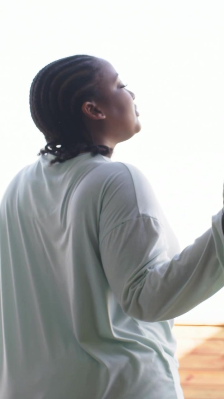 Vertical video: Sunlight drawing woman turning toward deck, holding door in light long-sleeve shirt