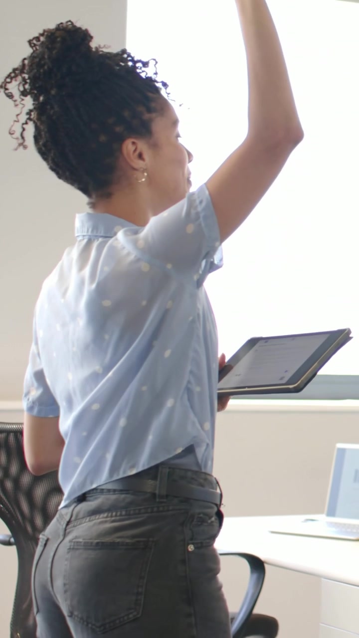 Video verticale: Uomo alla scrivania con tazza che inizia a parlare e gesticola, donna in top blu che tocca i grafici sul tablet.