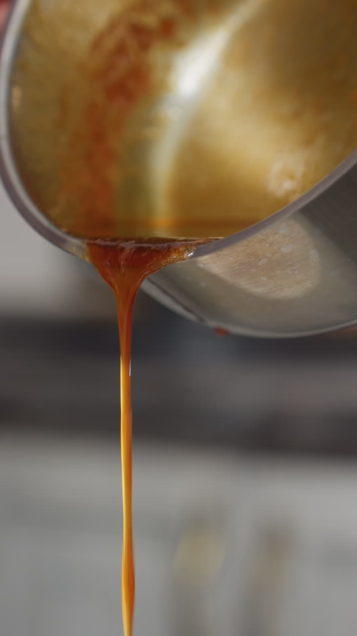 Partial view of person in plaid clothing pouring rich red soup from stainless pot while stirring, thick liquid flows smoothly as cook prepares homemade meal in modern kitchen