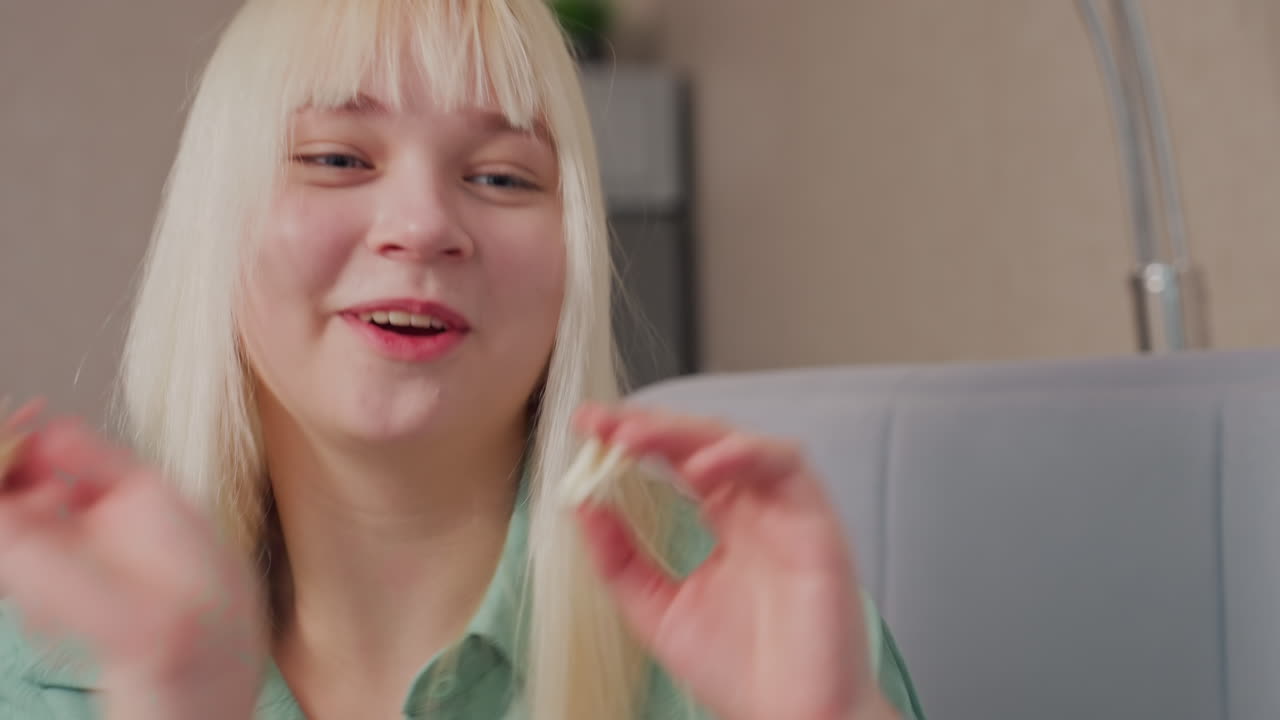 Close up of smiling blonde girl in green shirt tossing popcorn at someone nearby in cheerful playful mood, her joyful expression and relaxed posture reflect lighthearted fun during indoor interaction