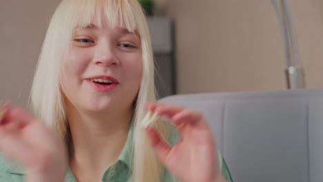 close up of smiling blonde girl in green shirt tossing popcorn at someone nearby in cheerful playful mood, her joyful expression and relaxed posture reflect lighthearted fun during indoor interaction