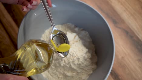 woman adding a spoon of oil to flour in a bowl