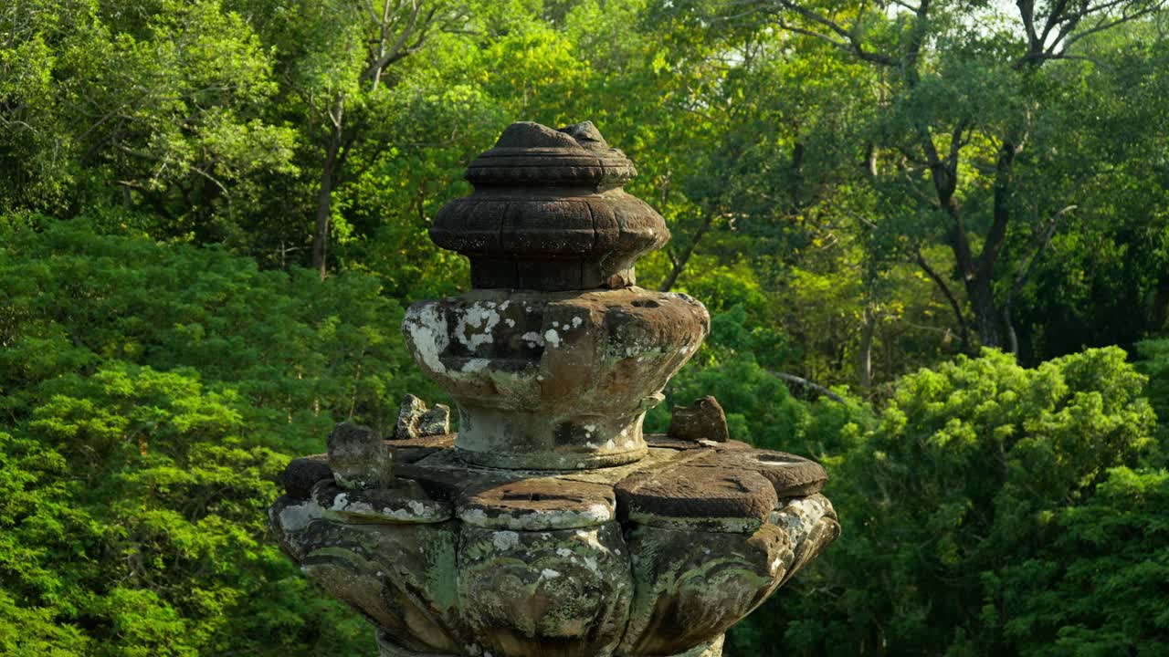 Ancient stone monument covered in moss rising above lush jungle in Angkor Thom