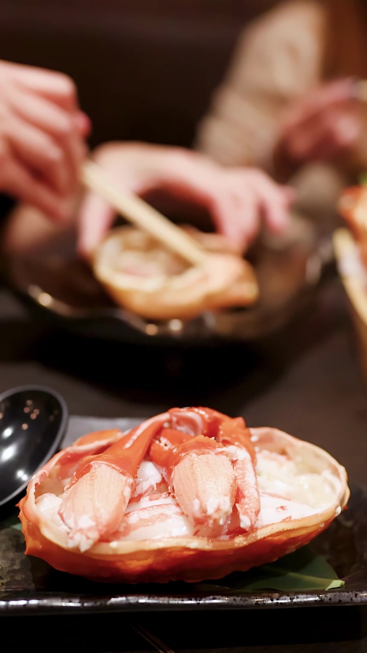 Primo piano di zampe di granchio nel guscio con commensali che usano le bacchette in un ristorante.
