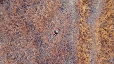 Woman-lying-in-dry-savanna-grass-in-Bali-captured-from-aerial-view