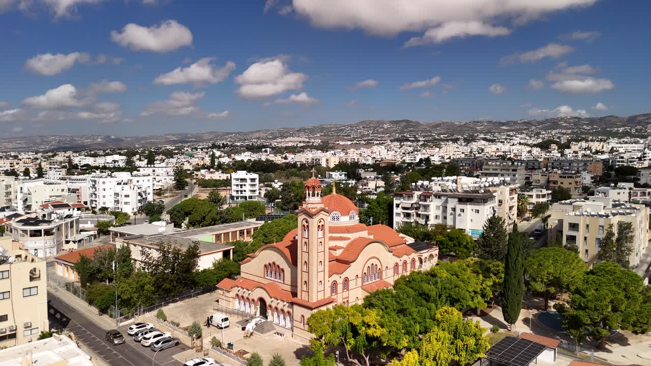 View the captivating skyline of Paphos, Cyprus, featuring the impressive Agios Nikolaos Church. Discover the charm of this city with green spaces and white buildings