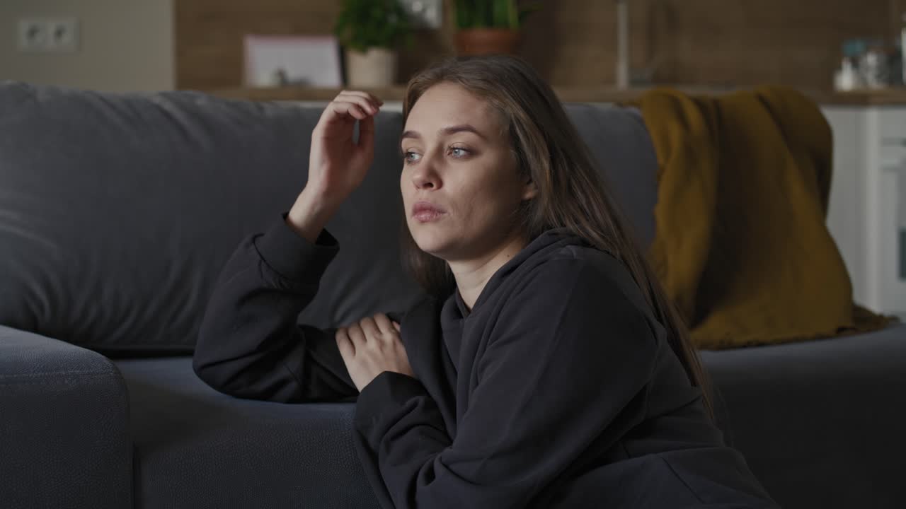 Caucasian young woman sitting at the floor and looking away with sad face.