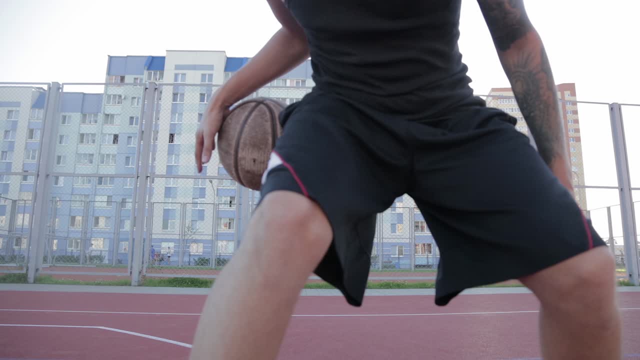 Man in black sportswear hits the ball on the playground on the background of residential buildings