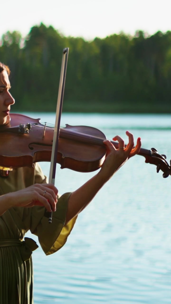 Woman Playing Violin Outdoors by a Lake at Sunset