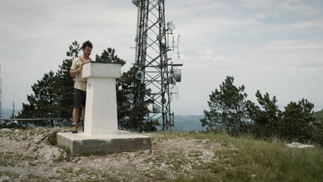 Hiker-with-an-orange-backpack-standing-by-a-concrete-monument-at-the-top-of-mountain-Slavnik-near-radio-tower