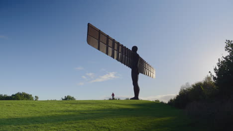 angel of the north against blue sky, silhouetted man walks along the path