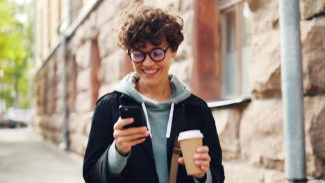 woman walking down the street, using a smartphone and drinking coffee
