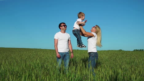 familia feliz: padre madre e hijo saltando y riendo en el campo con camisetas blancas y vaqueros