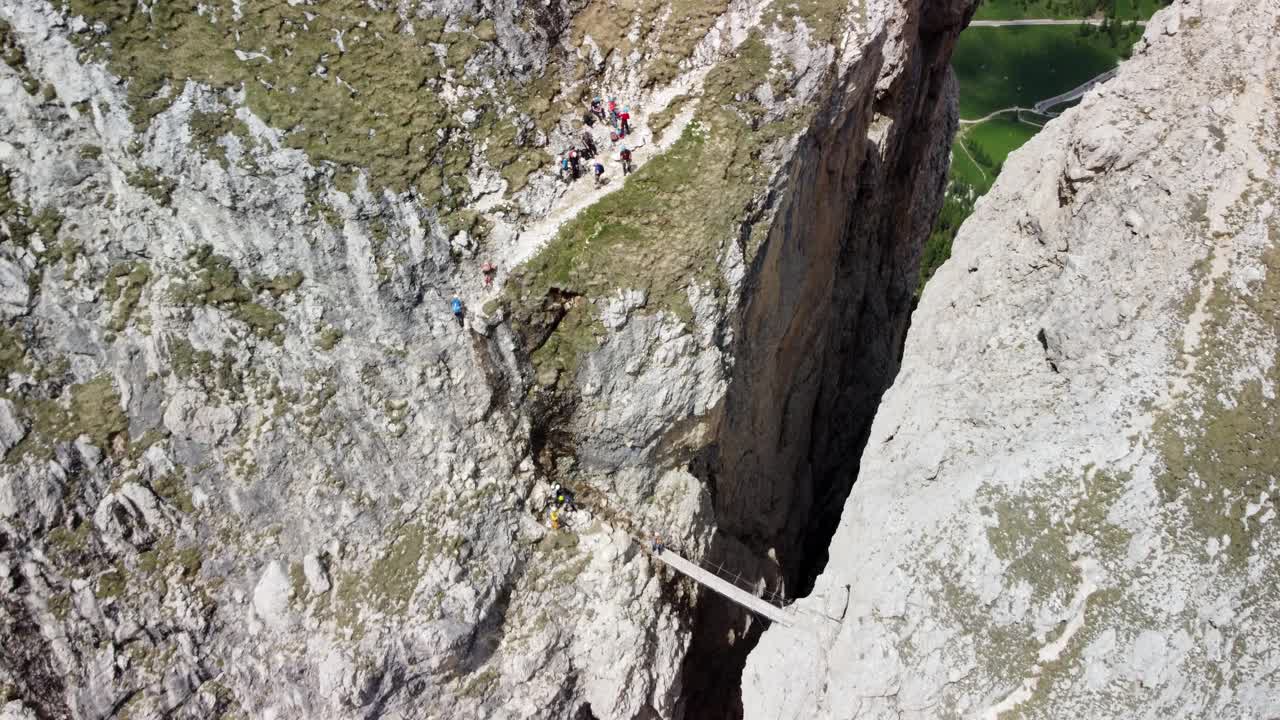 Hikers crossing a narrow wooden bridge between two cliffs in the Dolomites. Dolomites, Italy