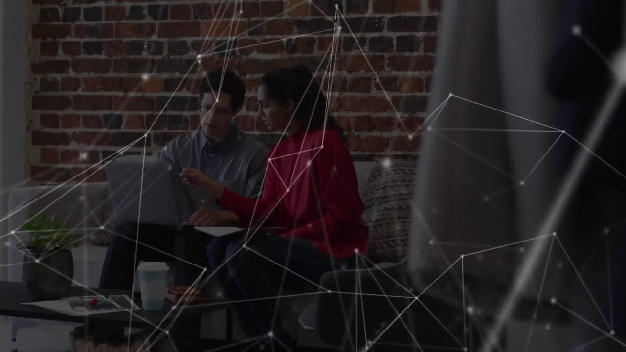 Animation of network over male and female colleague using laptop on couch in office