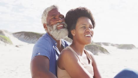Happy-african-american-couple-sitting-and-embracing-on-sunny-beach