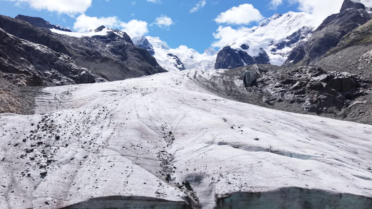 Drone ascends steep glacier wall revealing frozen riverbed and rocky plateau
