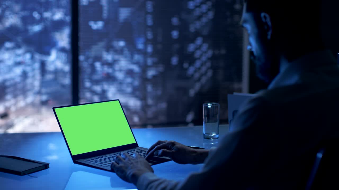 à noite, o empresário trabalha num portátil com ecrã verde no seu escritório privado com vista para a grande cidade.