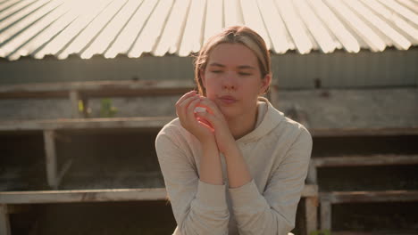 close-up of a thoughtful woman in casual attire sitting on rustic stadium bleachers, hands joined together, her expression reflects deep contemplation