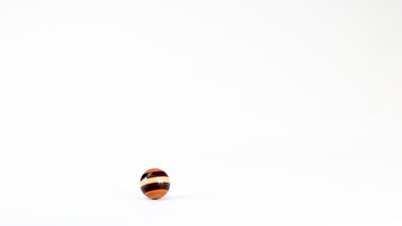 A small striped wooden bead falls, bounces, and rolls across a clean white surface