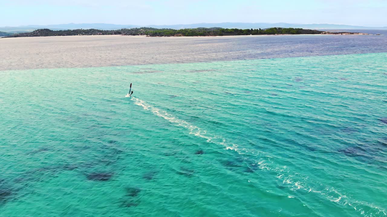 Aerial drone view of a man at windsurfing in Aegean sea. Transparent water, land with greenery in Greece