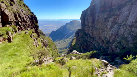 Ruta-De-Senderismo-Entre-Acantilados-Cima-Del-Mundo-Montaña-De-La-Mesa-Ciudad-Del-Cabo-Sudáfrica-Góndola-Impresionante-épica-Mañana-Ver-El-Centro-De-La-Ciudad-Caminata-De-Cabeza-De-León-Exuberante-Primavera-Verano-Hierba-Flores-Verde-Pan-A-La-Izquierda