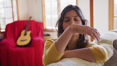 Portrait-of-happy-mixed-race-woman-leaning-on-sofa-smiling-n-sunny-living-room