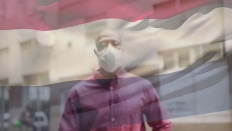 Animation-of-flag-of-netherlands-waving-over-african-american-man-wearing-face-mask-in-city-street