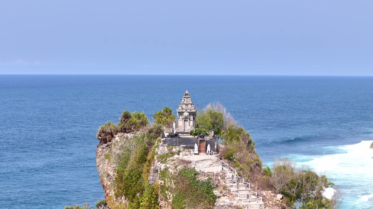 Incredible landscape of Javanese temple on the cliff formed by coral, in the background the calm sea and the blue sky merging into the horizon. Video shot on Ngobaran beach, Indonesia.