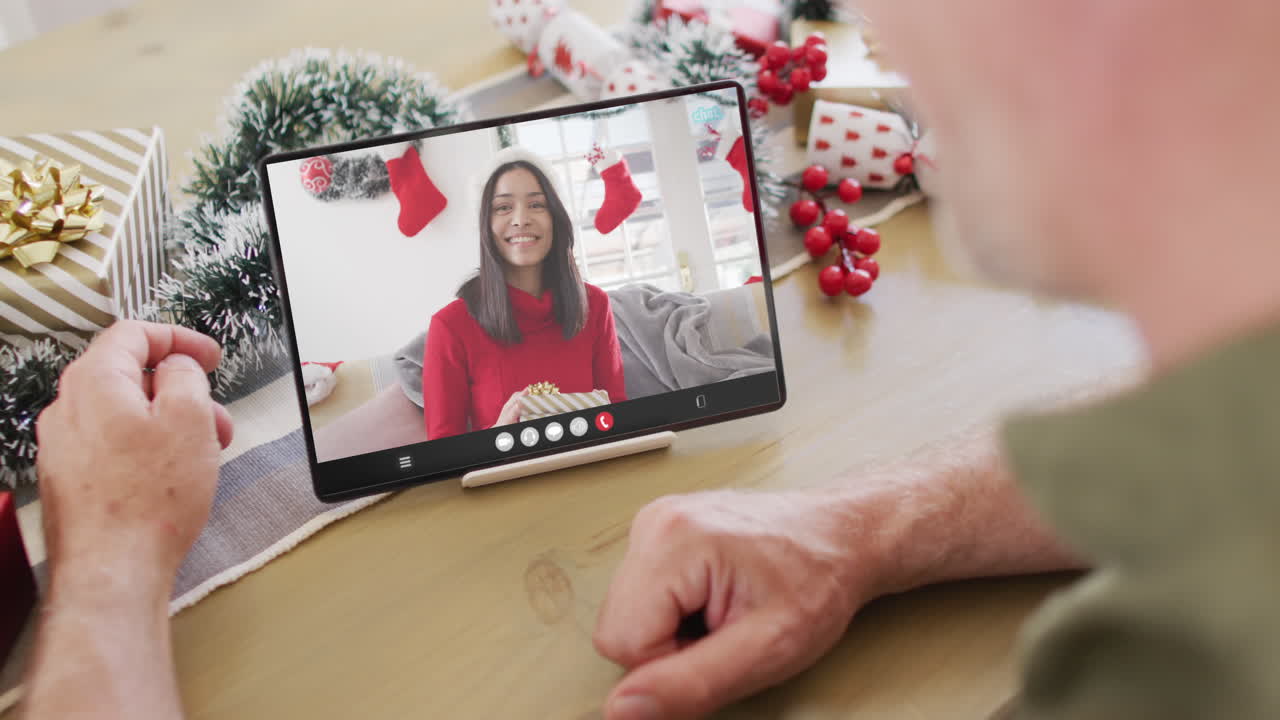 hombre caucásico con decoraciones navideñas teniendo una llamada de video de tableta con una mujer biracial