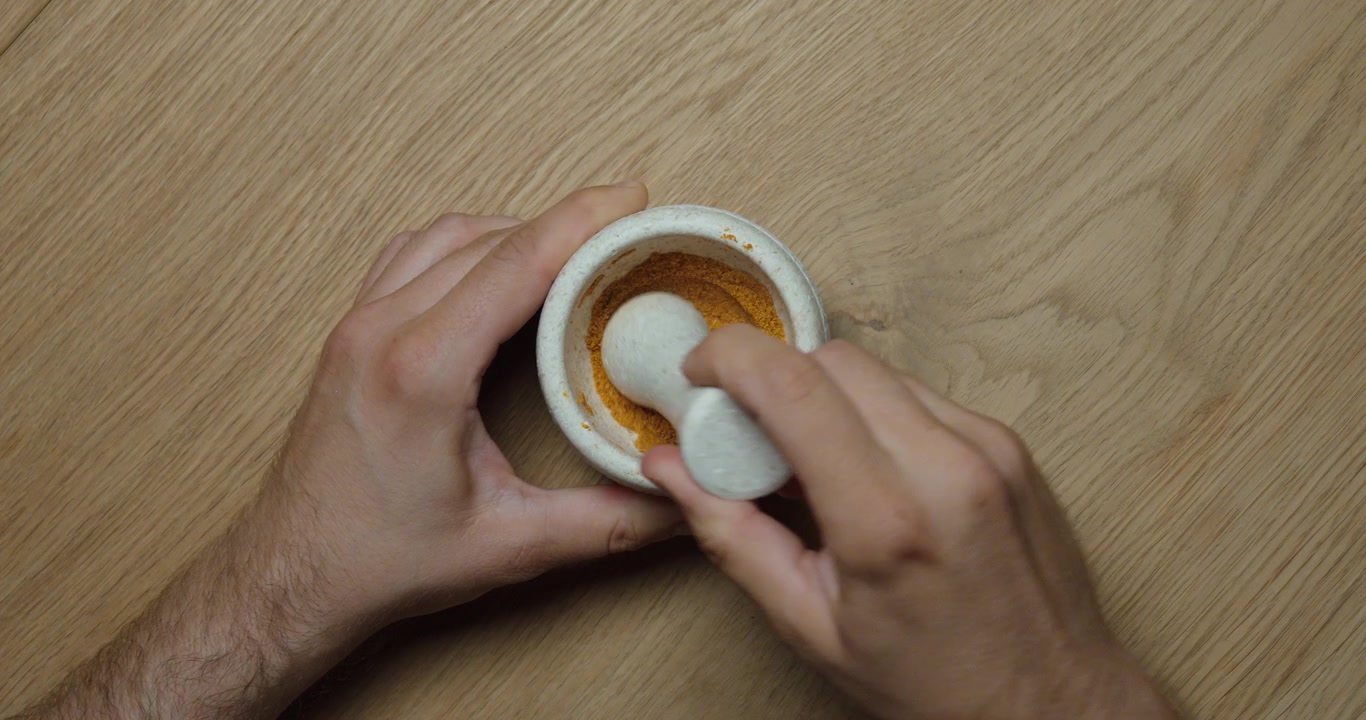 Vista dall'alto di una persona che macina spezie con mortaio e pestello. Concetto di preparazione del cibo, cucina, ingredienti freschi e tecniche culinarie tradizionali.