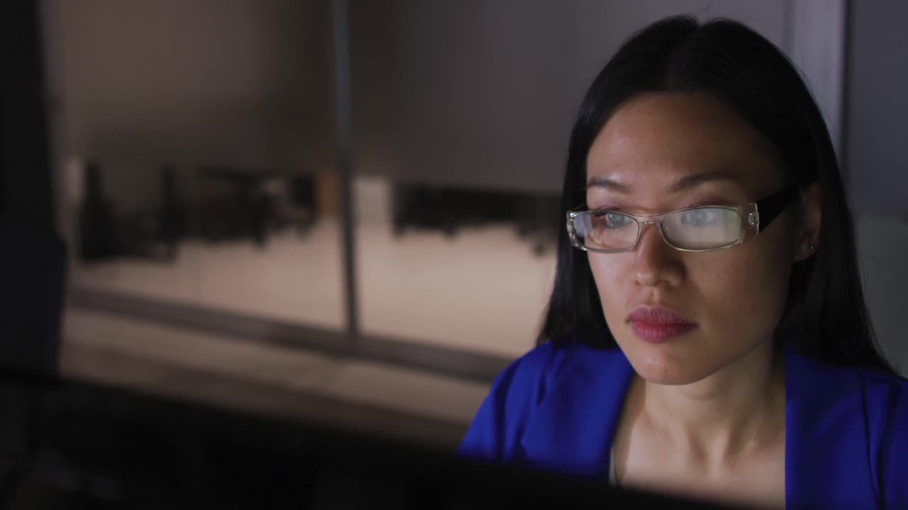 video de una mujer de negocios asiática con gafas mirando la pantalla de la computadora, trabajando de noche en la oficina