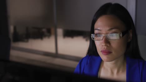 Video-of-asian-businesswoman-in-glasses-staring-at-computer-screen,-working-at-night-in-office