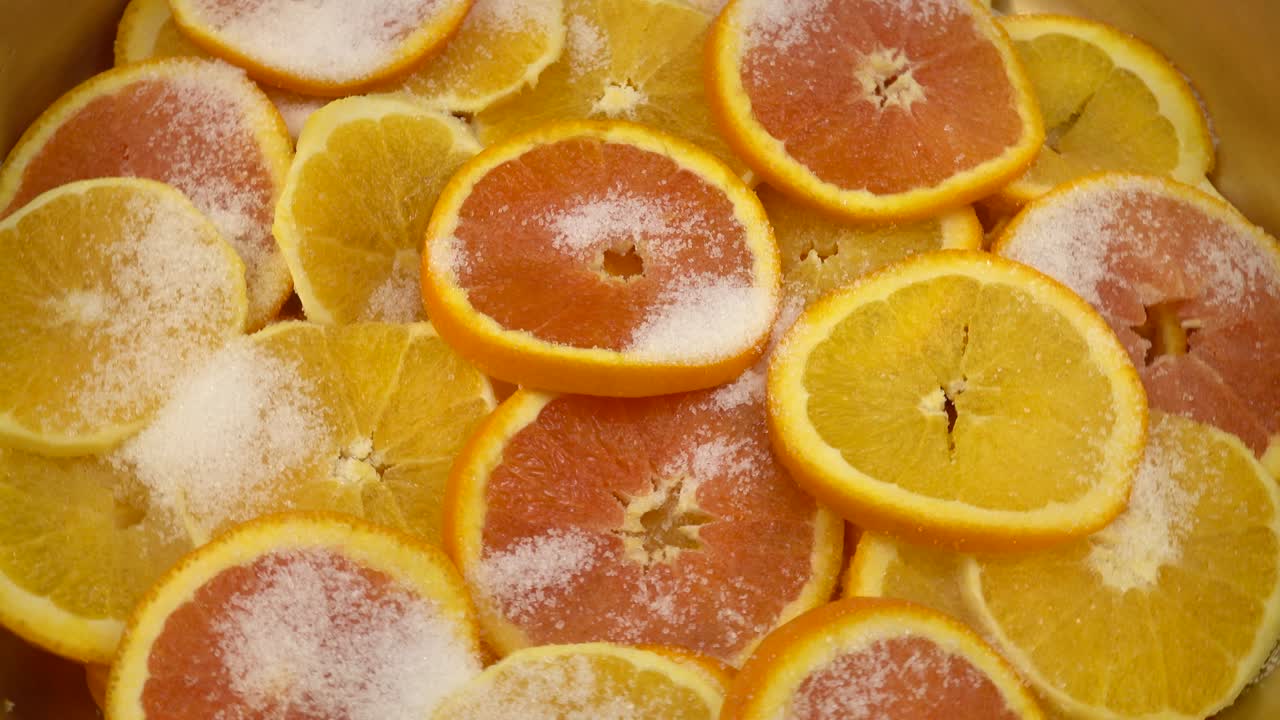 Orange slices sprinkled with sugar lie in layers in a copper basin for making jam.