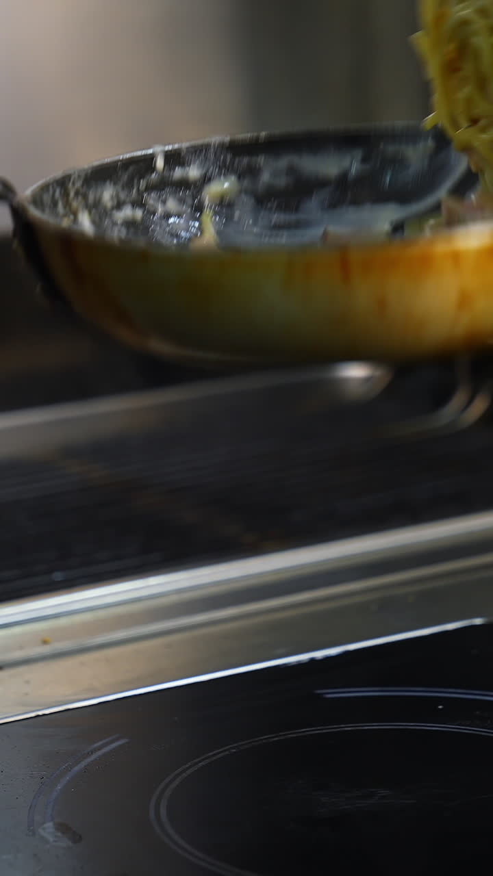 Cooking meals in a restaurant. Chef is cooking dish in a frying pan and flipping throwing it. Cooking the spaghetti in white sauce in the frying pan. Close-up. Vertical video
